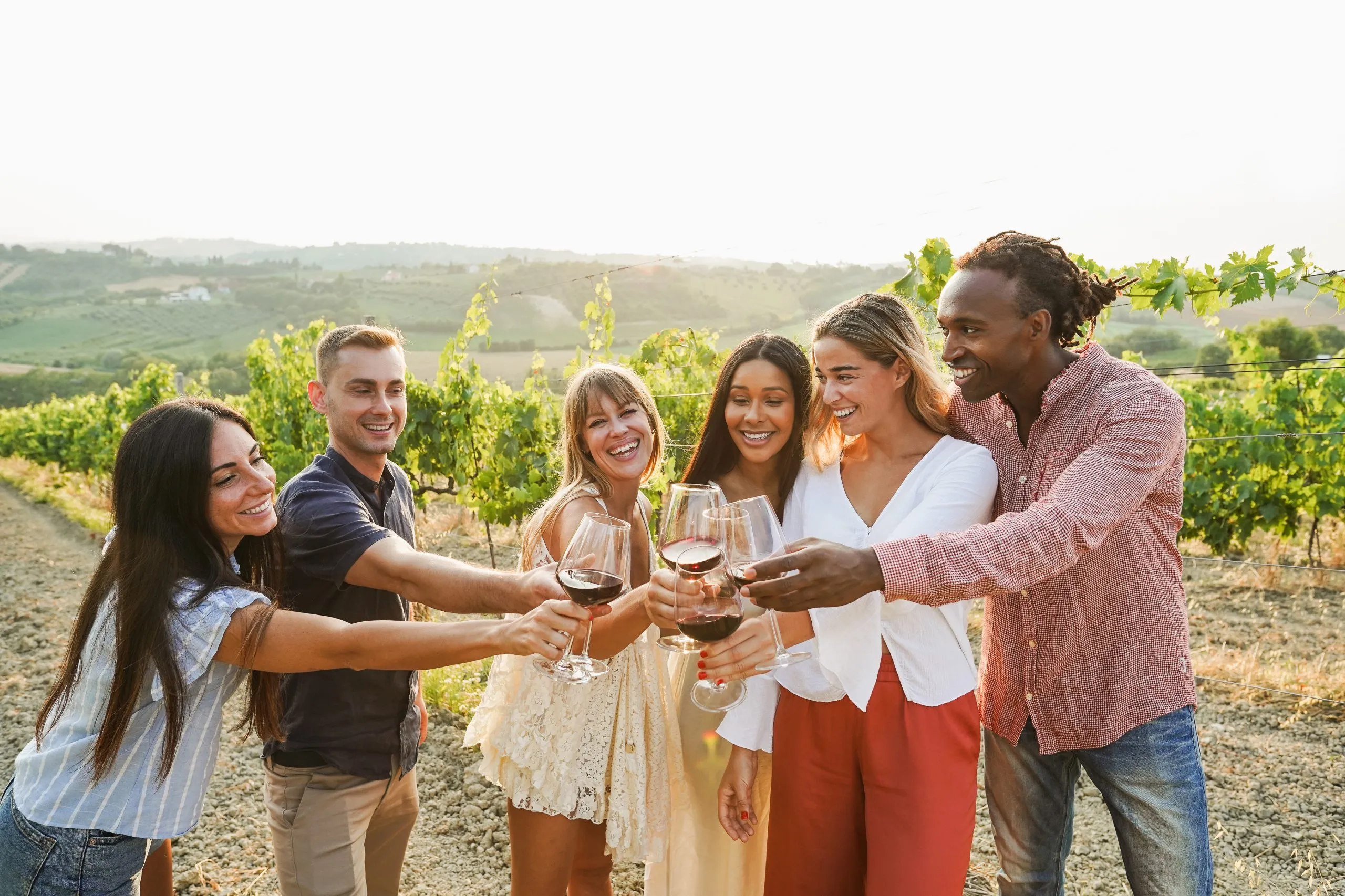 Amigos felices animando con vino tinto en un evento de verano en el campo - Gente multirracial divirtiéndose durante unas vacaciones gastronómicas - Concepto de viaje, vacaciones y degustación de productos tradicionales - Enfoque en los rostros